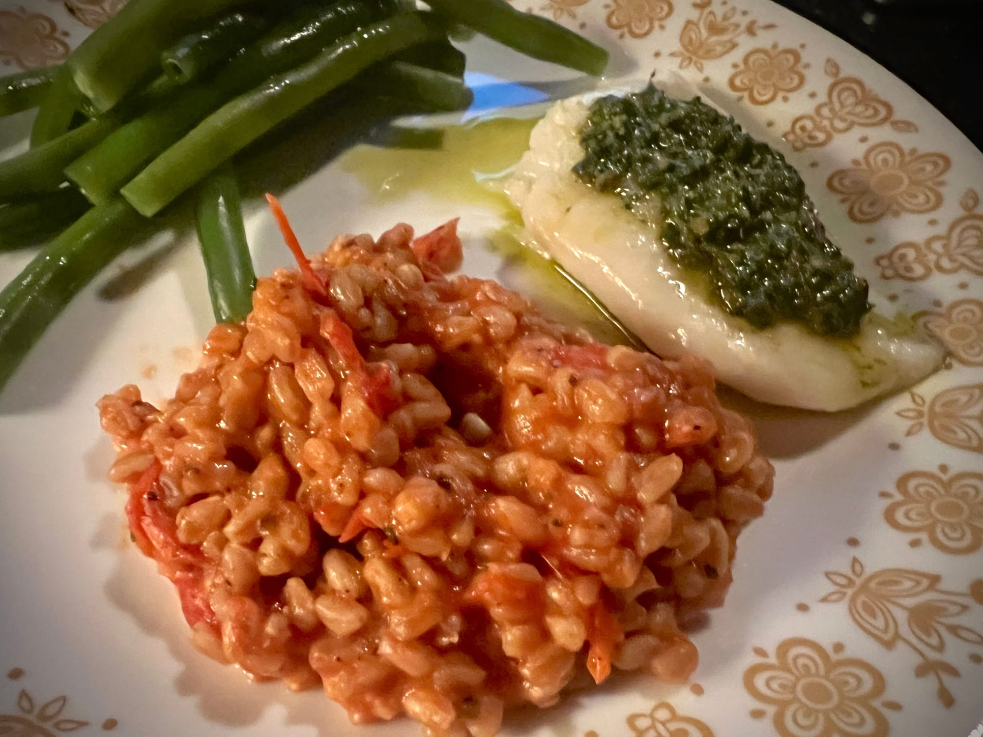 A lumpy mound of farro & tomatoes is on a plate, beside a white piece of fish & green sauce, and a pile of long green beans.