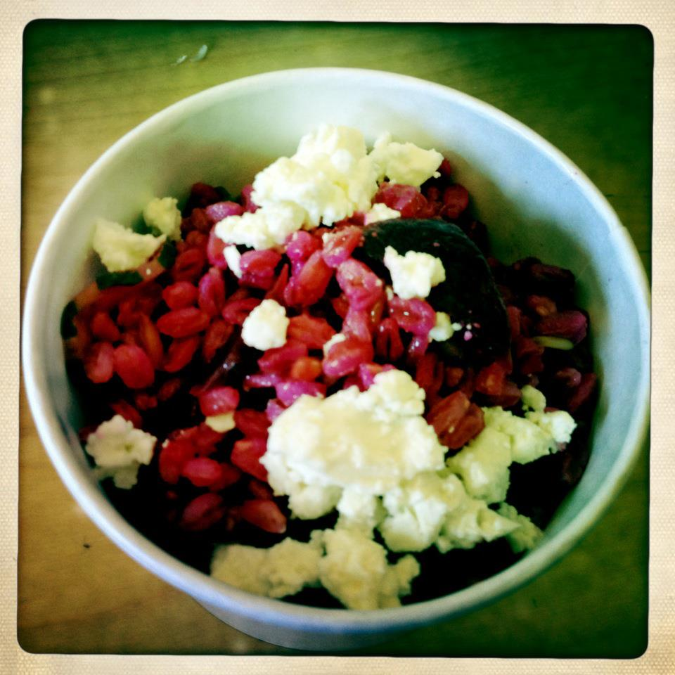 Pink farro is tossed with bright white crumbles of feta, in a white paper to-go container.