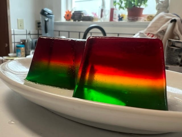 Two cubes of Jell-O. It has three color layers: red, yellow, and green.