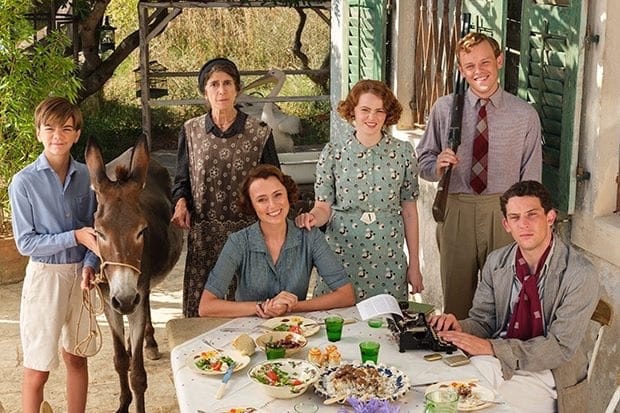 A family is gathered around an outdoor dining table, smiling. The youngest child has a donkey.