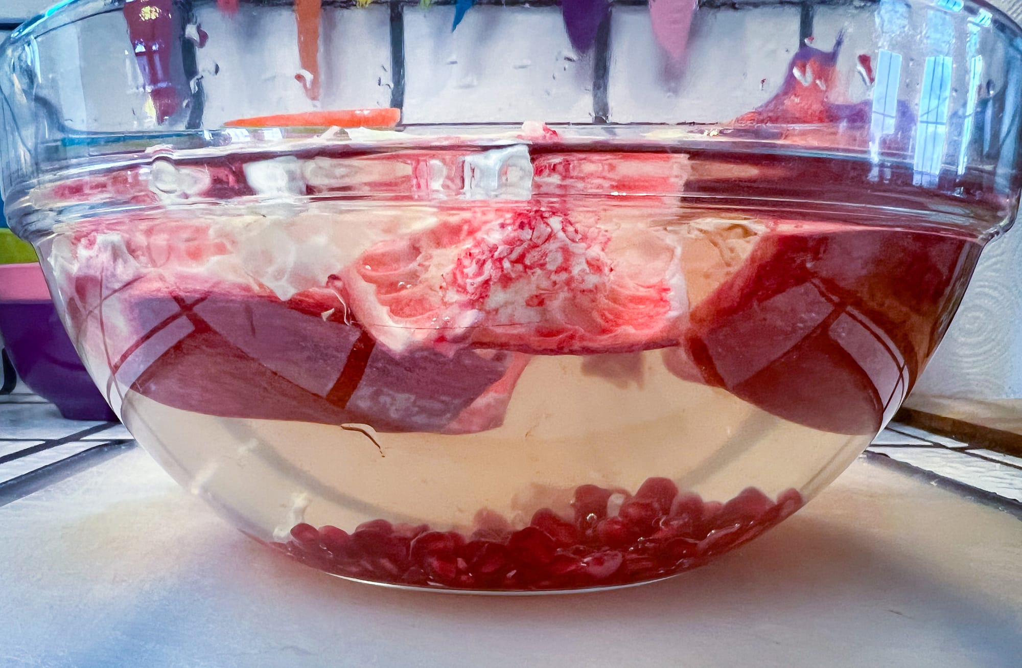 Side view of the glass bowl. White and red hunks of the rind and membrane are floating at the top, and small, red seeds are sitting at the bottom.