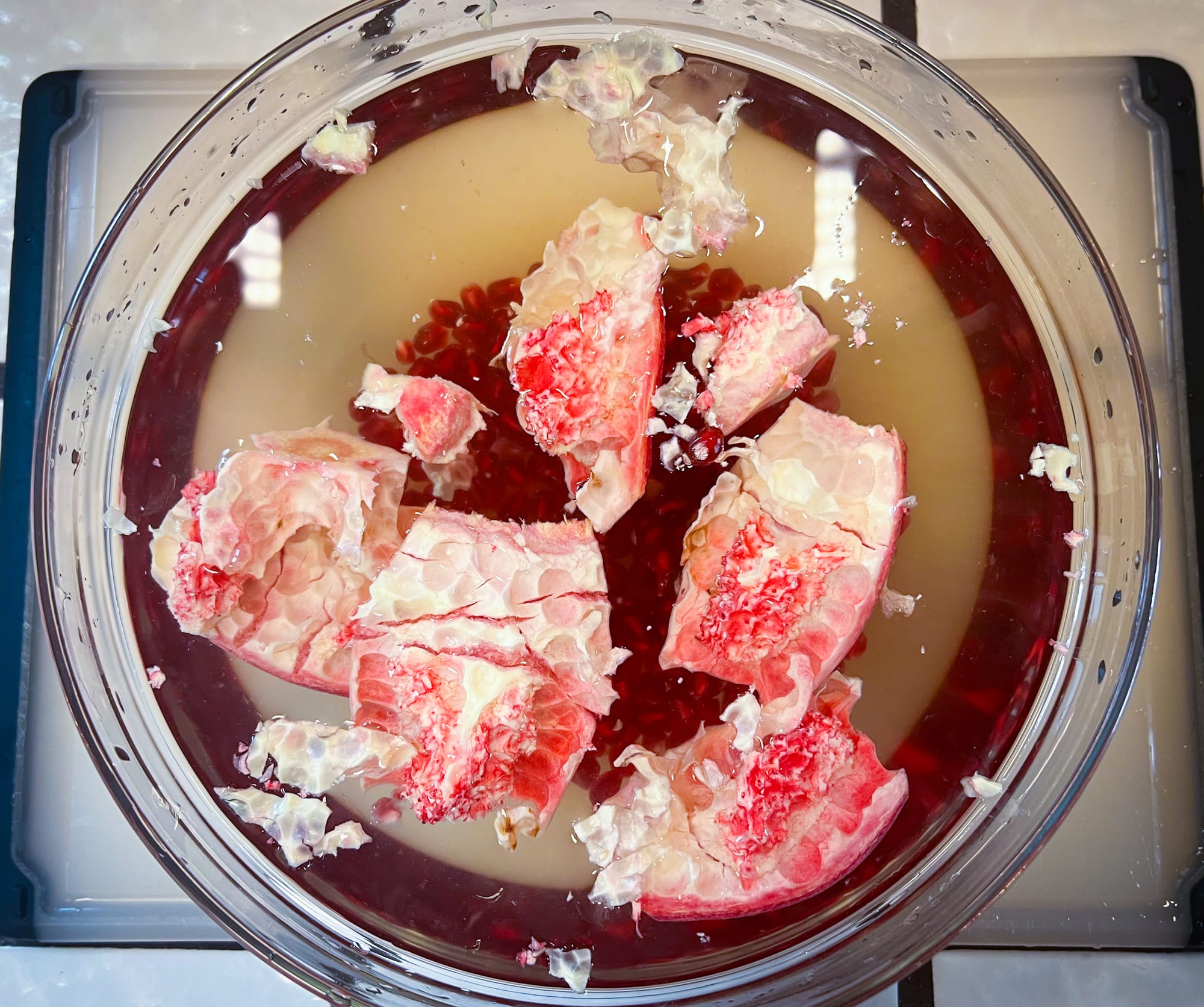 Top view of the glass bowl. White hunks of the rind and membrane are floating at the top, and small, red seeds are sitting at the bottom.