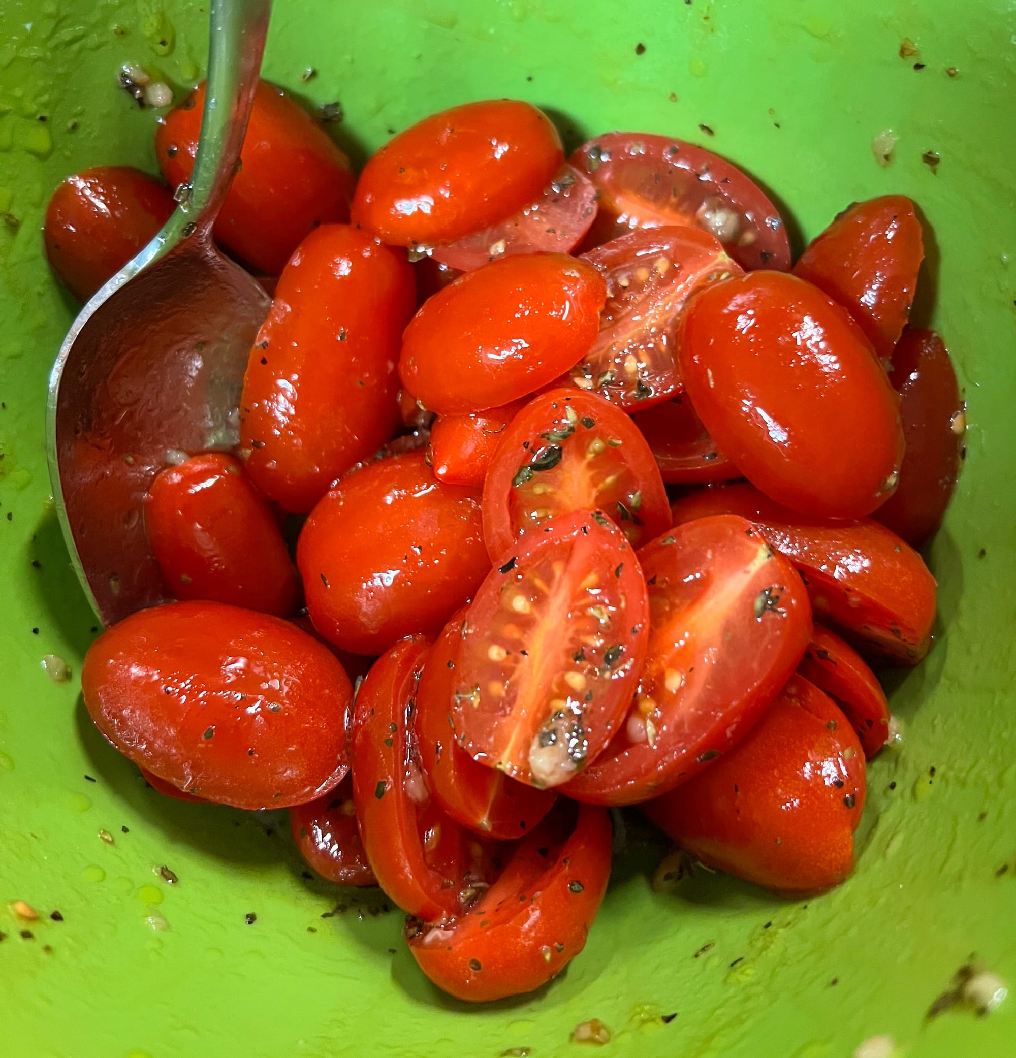 Halved cherry tomatoes are seen in a bowl, where they've been dressed with olive oil and herbs.