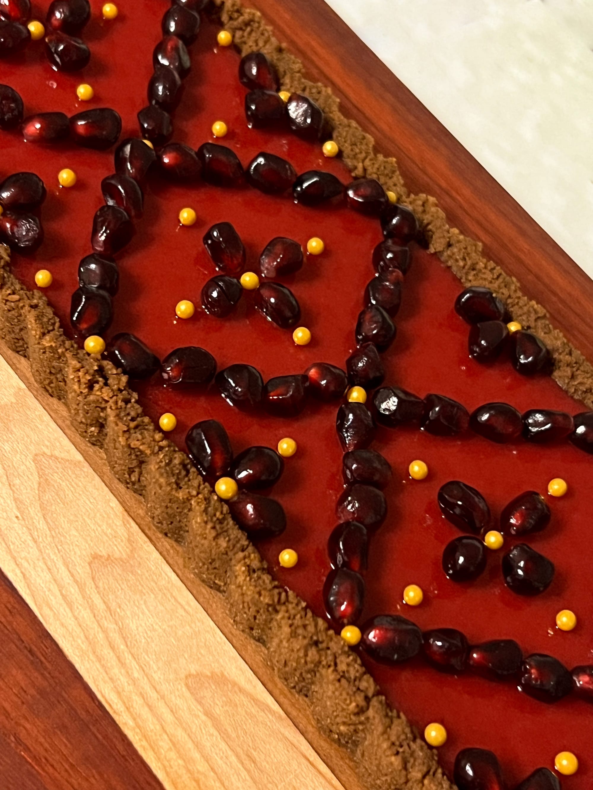 A rectangular tart with bright, deep pink custard is studded with pomegranate seeds in a decorative geometric pattern