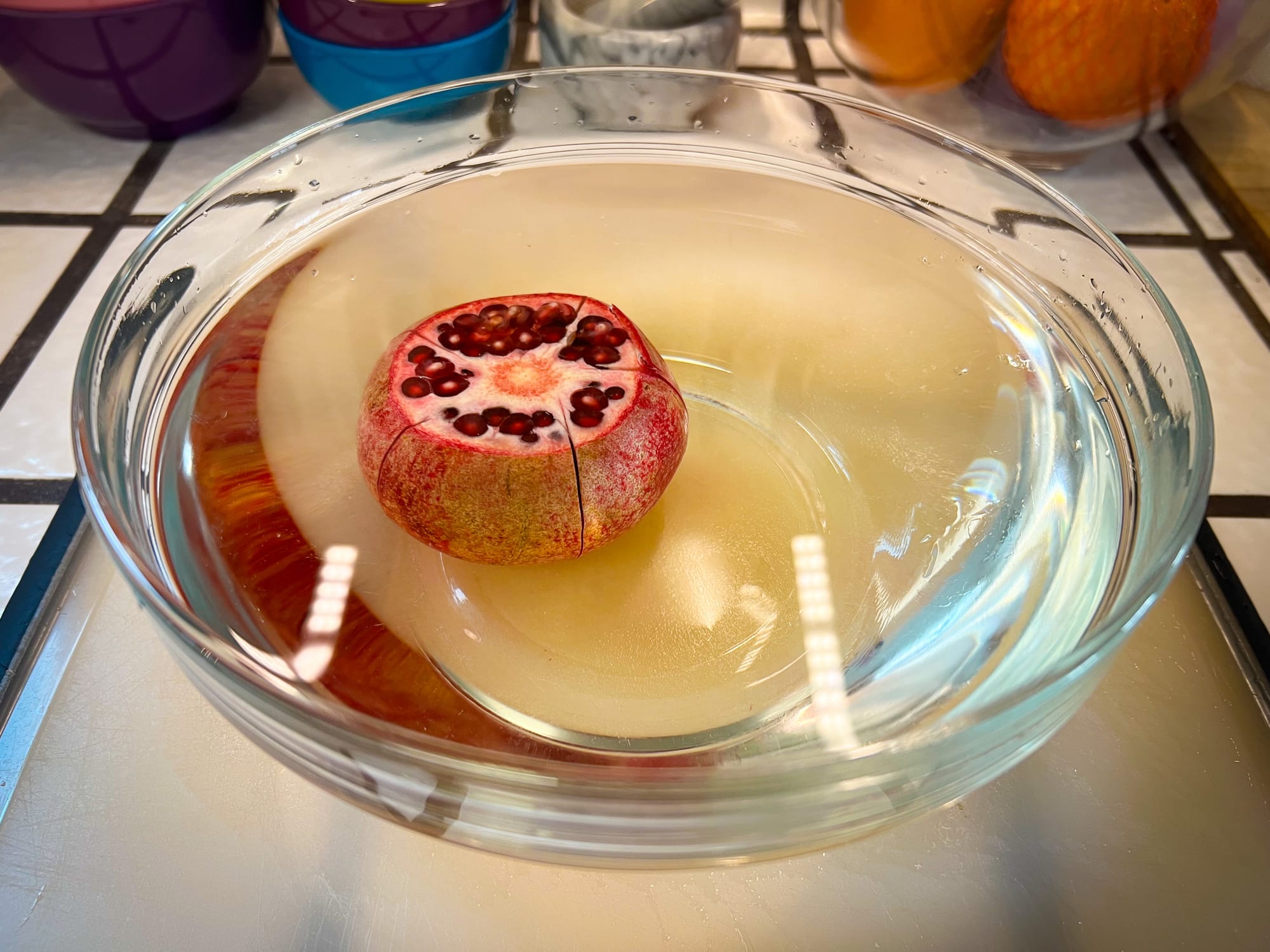 The pomegranate is now submerged in a large glass bowl filled with water. You can see five of those vertical cuts have been made around the outer edge.