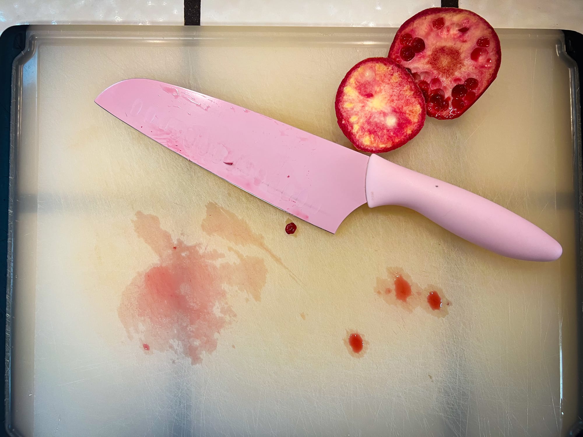 A cutting board has a very small bit of bright red pomegranate juice, and there is a slightly dirty knife, and the top and bottom slivers of the pomegranate. Very quick cleaning.