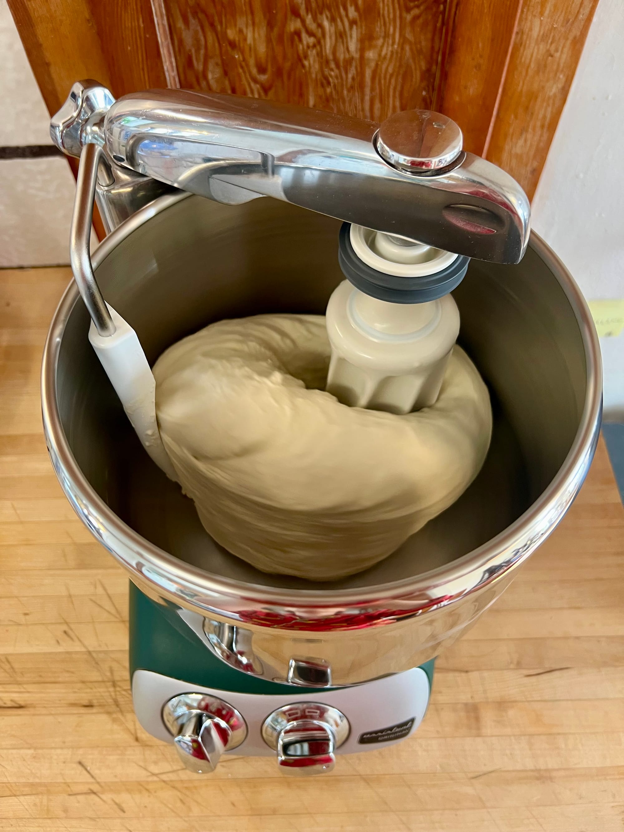 Overhead view of a large mixer, with dough being kneaded inside the bowl.