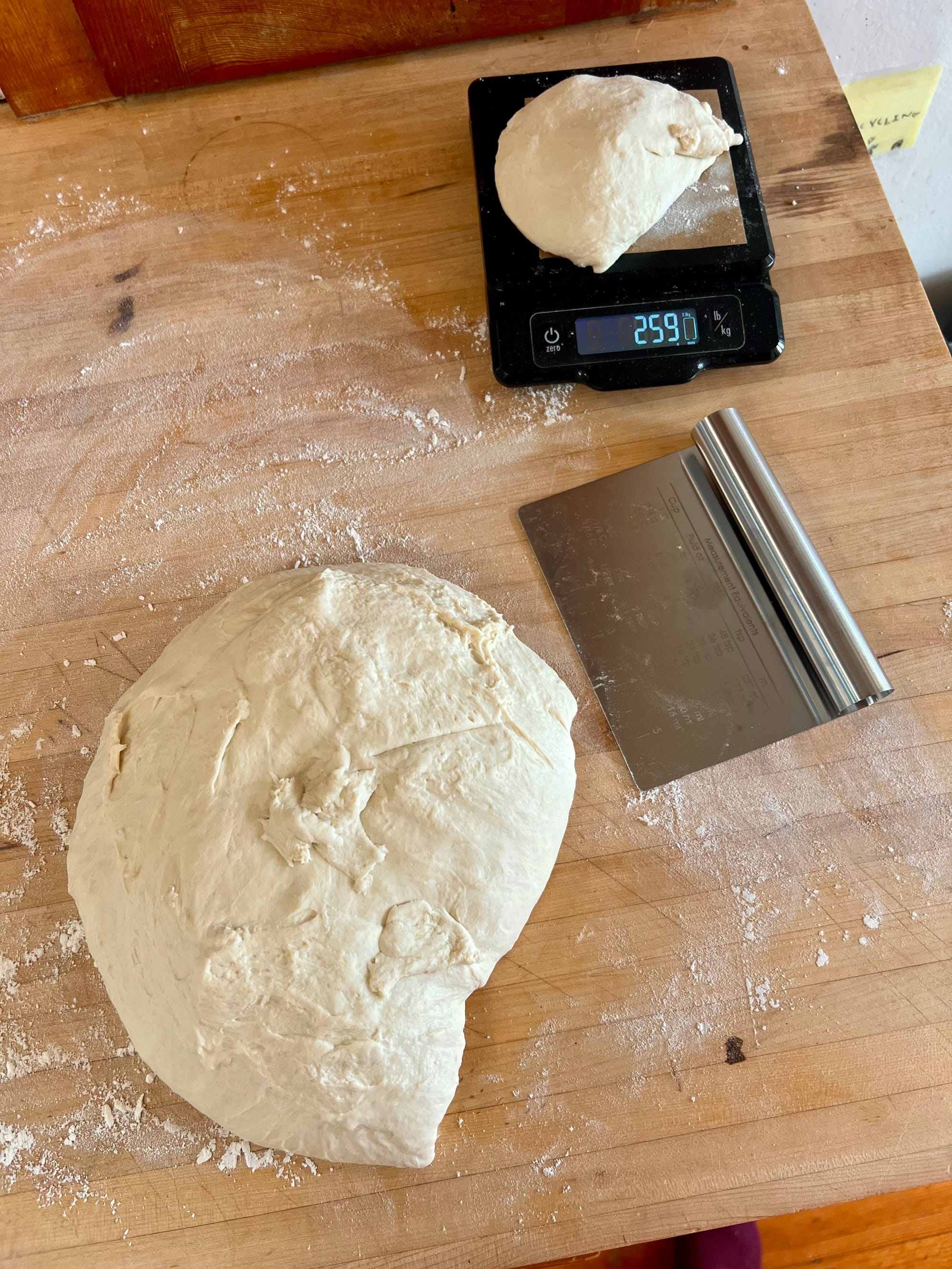 A large mass of dough is on a floured countertop, and a smaller lump of dough is on a scale reading 259.