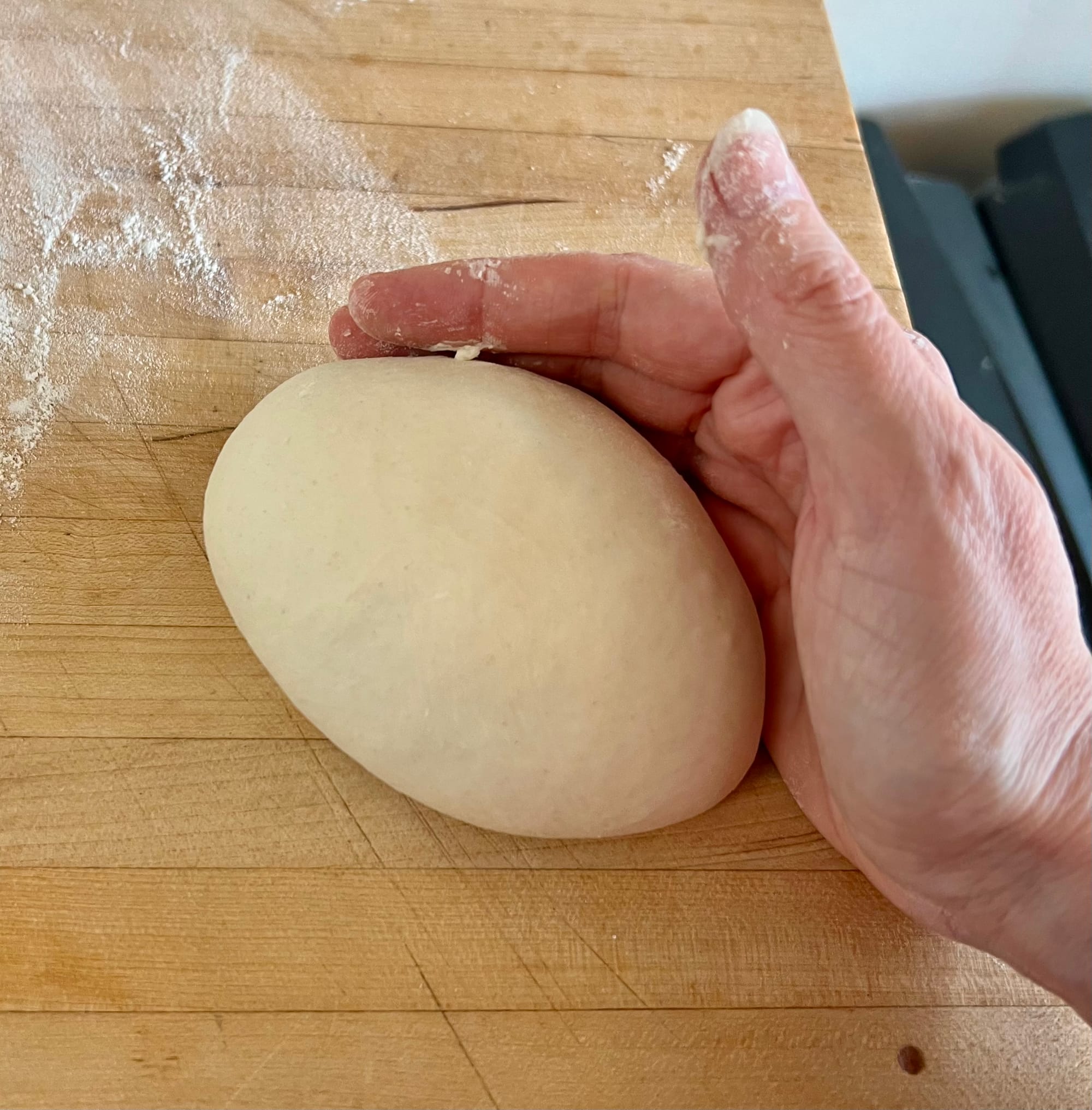 A hand is cupped around a ball of dough that is getting shaped into a smooth ball.