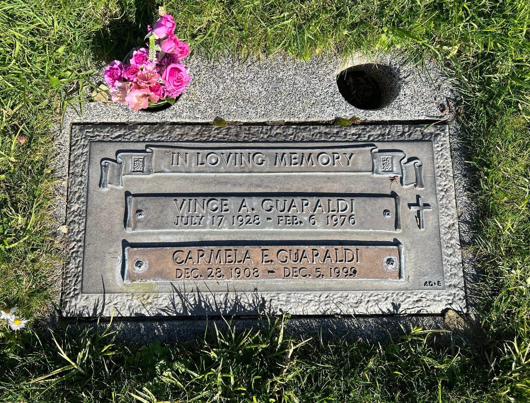 A metal plaque is flush with the grass ground around it. It says "In Loving Memory - Vince A. Guaraldi, July 17 1928-Feb 6 1976, Carmela E. Guaraldi, Dec 28 1908 - Dec 5 1999"