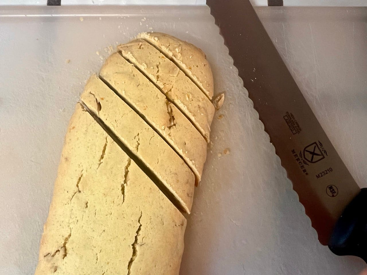 One of the logs is being cut on a cutting board with a serrated bread knife. The cuts are diagonal, to get an elongated cookie.