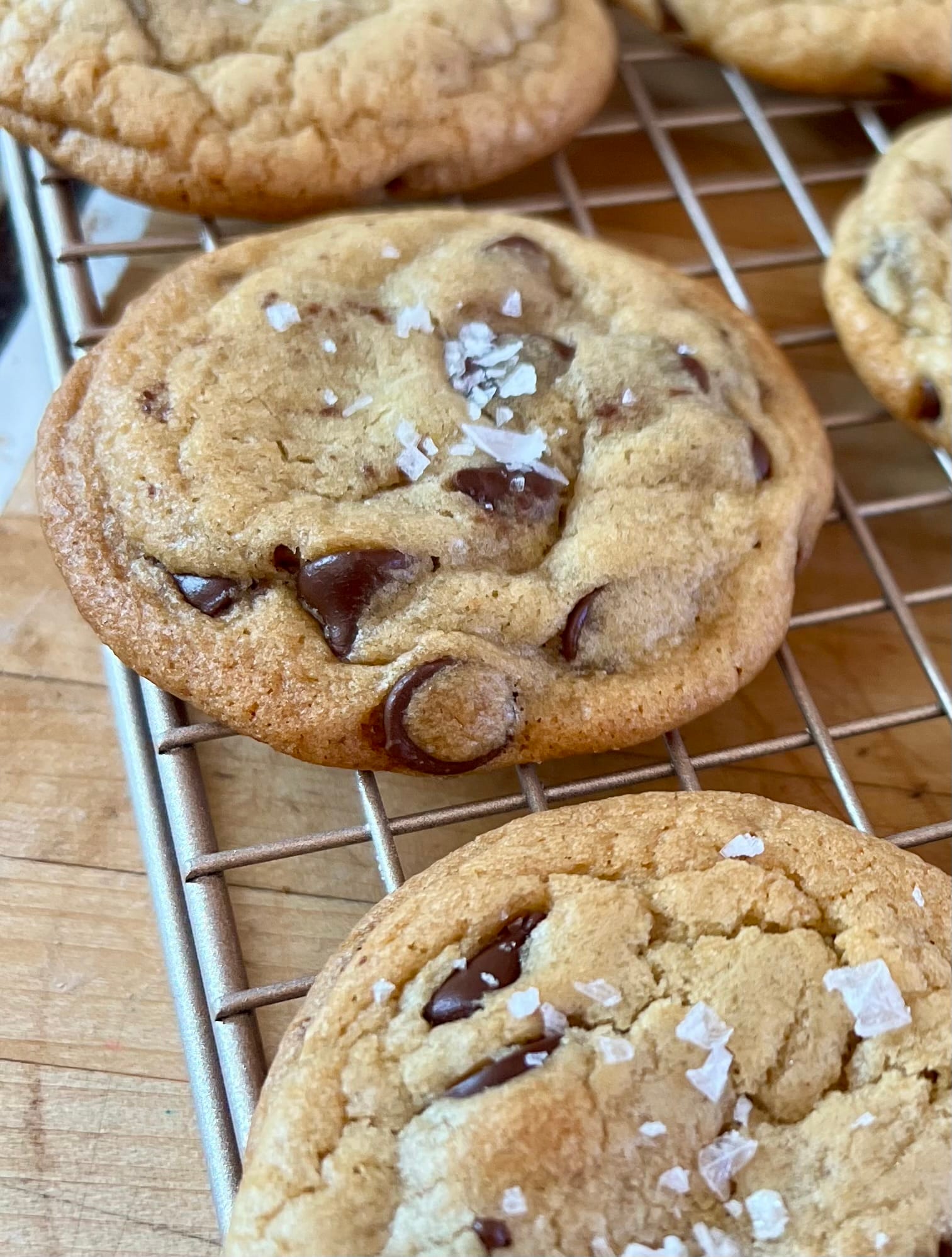 Chocolate chip cookies, topped with big flakes of salt, on a cooling rack.