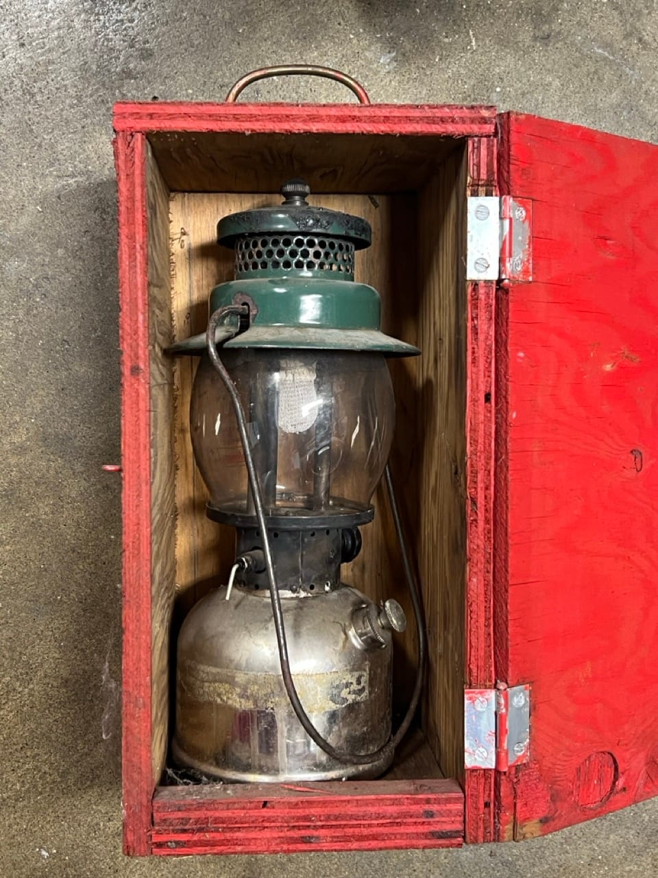 A very old kerosene lantern, inside of a red plywood box.