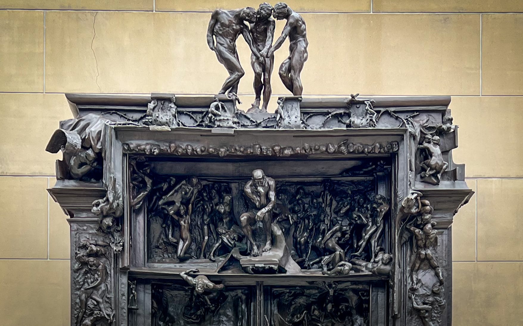 A nearly-black bronze sculpture of a doorway encrusted with writhing, nude human figures, w/a small version of The Thinker.