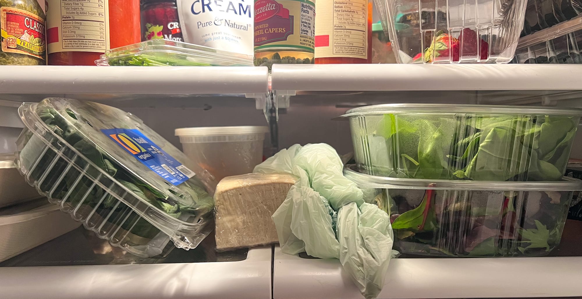 Shelves in a refrigerator, with leafy green produce and a block of tofu.