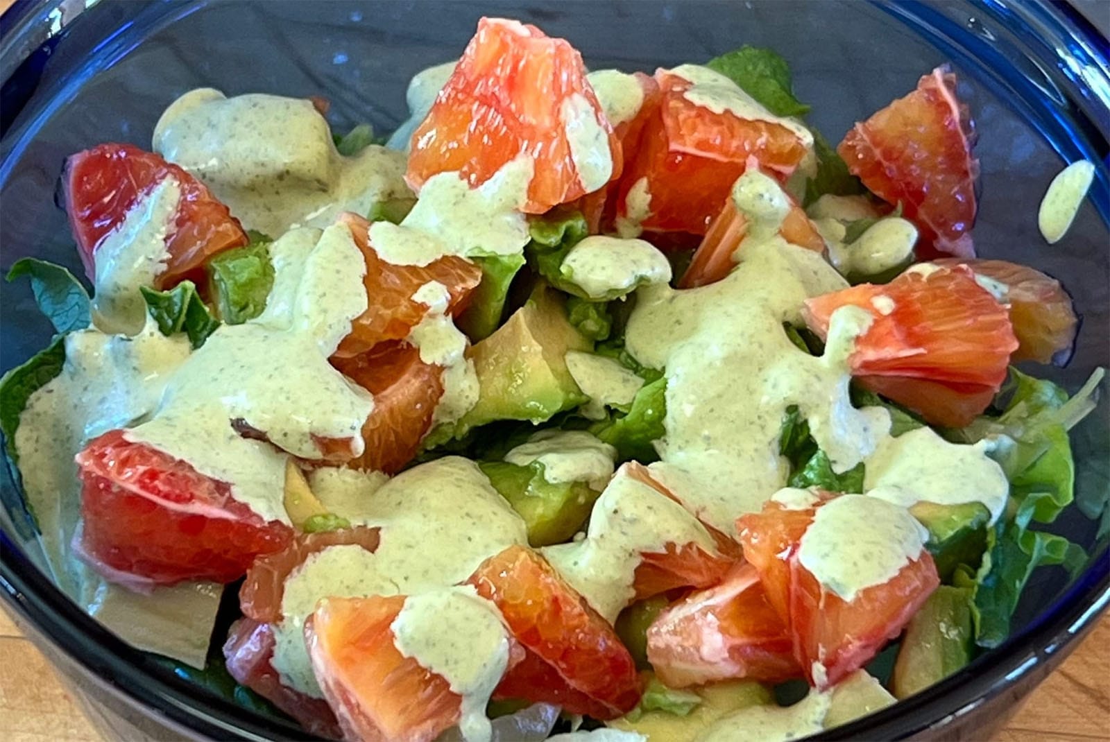 Bowl with salad greens, chunks of avocado and pieces of blood orange, topped with a bright green dressing.