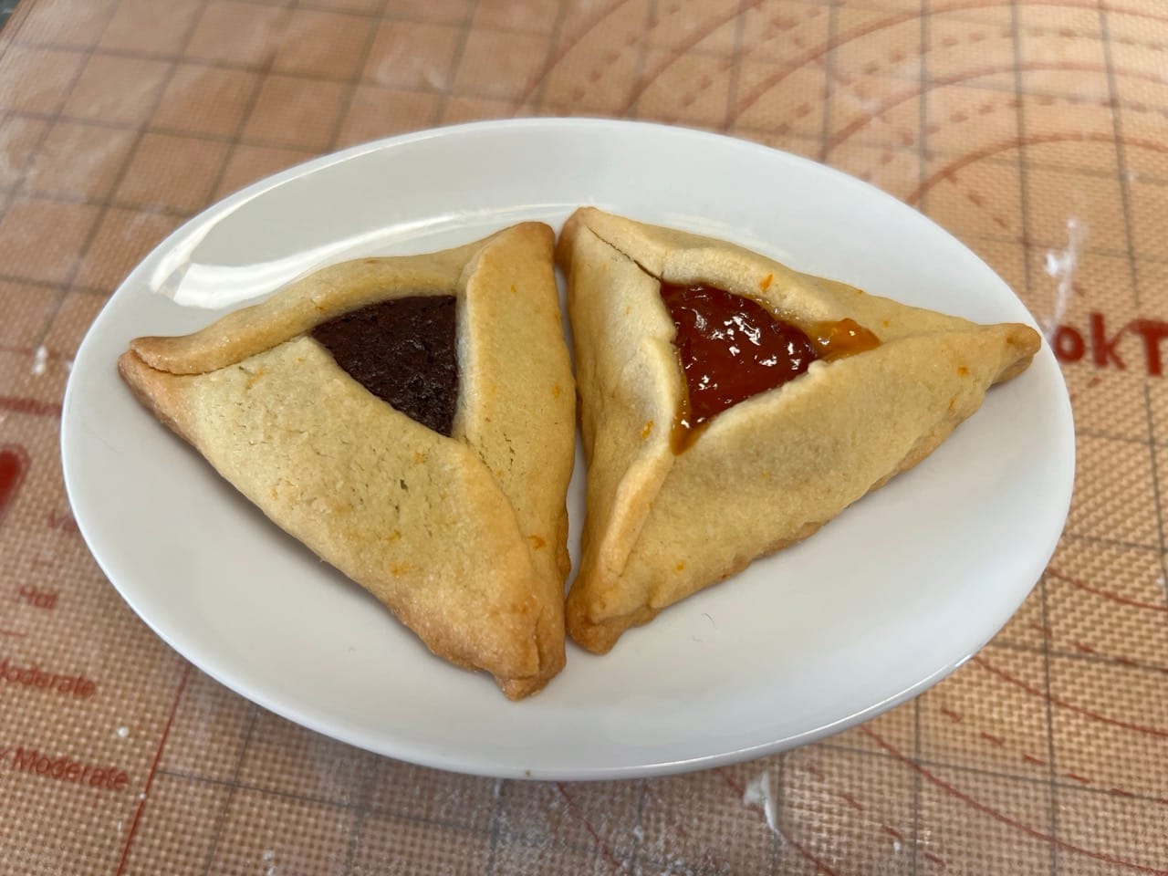 Two triangular cookies on a plate, one has chocolate filling, the other has apricot filling.