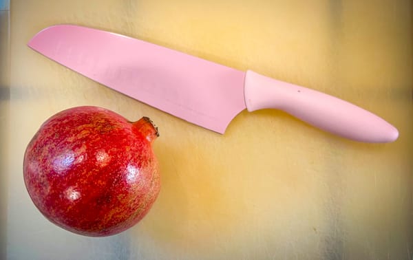 A pomegranate and a knife on a cutting board.