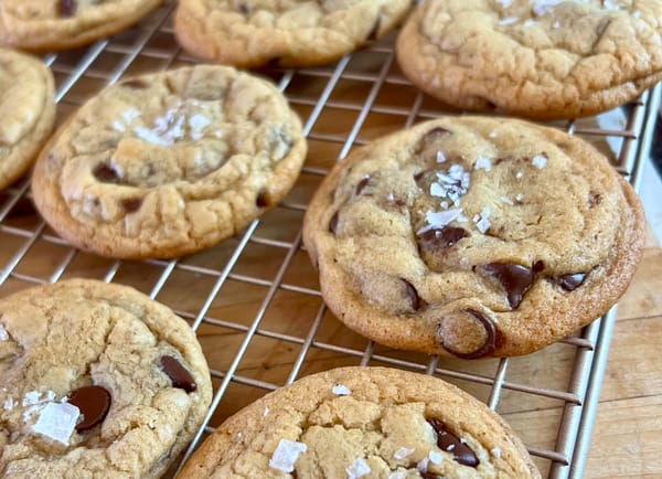 Chocolate chip cookies, topped with big flakes of salt, on a cooling rack.