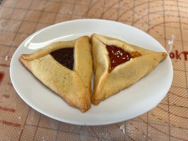 Two triangular cookies on a plate, one has chocolate filling, the other has apricot filling.